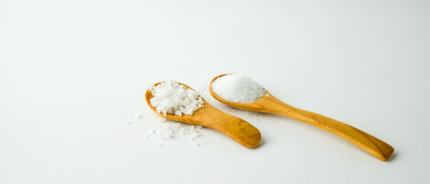 salt and sugar on small wooden spoon on white background