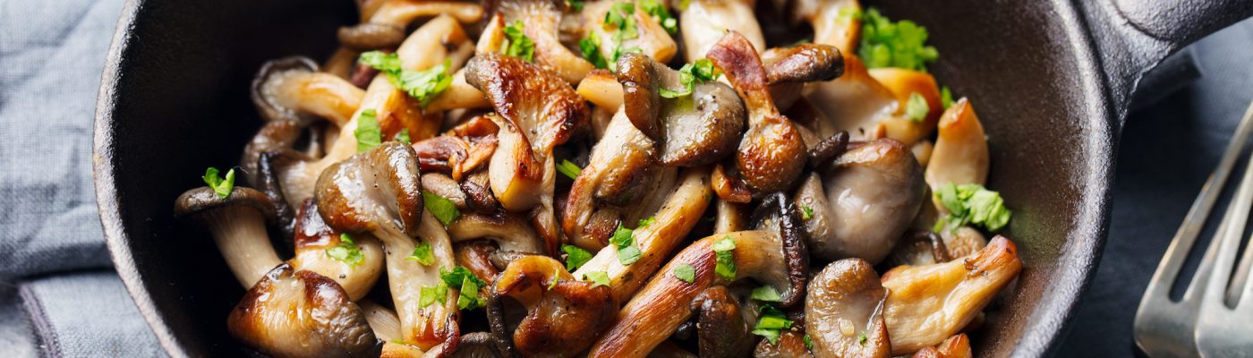 Fried mushrooms with fresh herbs in black cast iron pan.