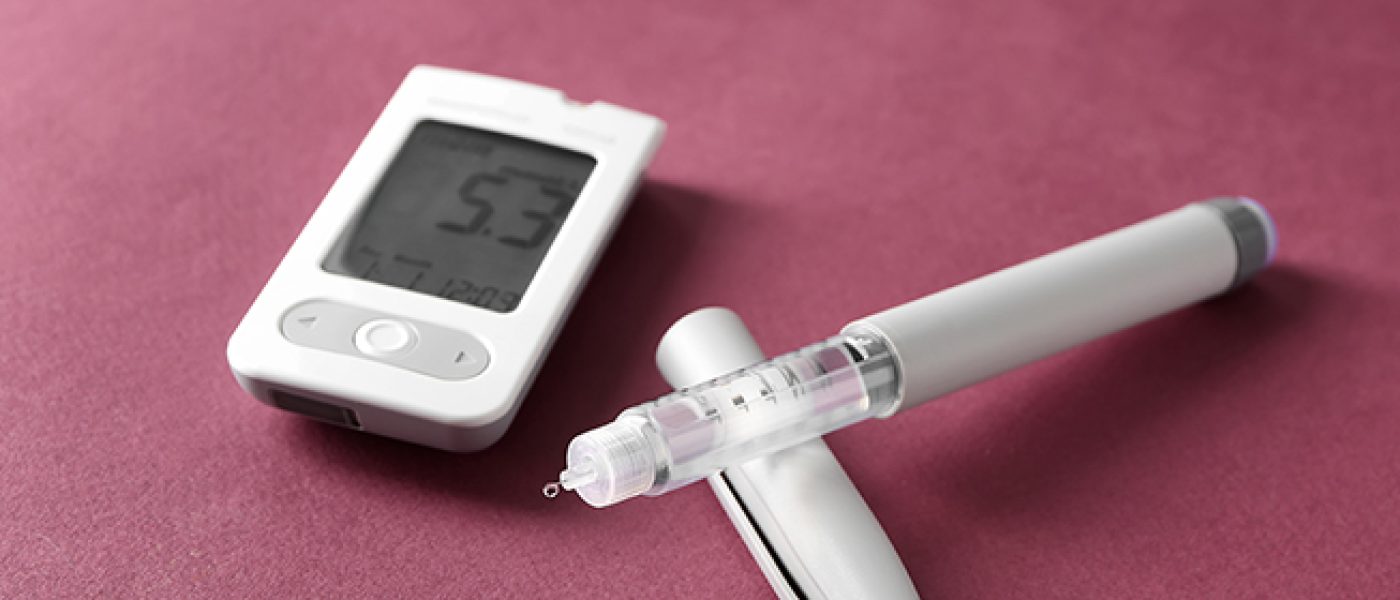 Digital glucometer with syringe on color background. Diabetes control