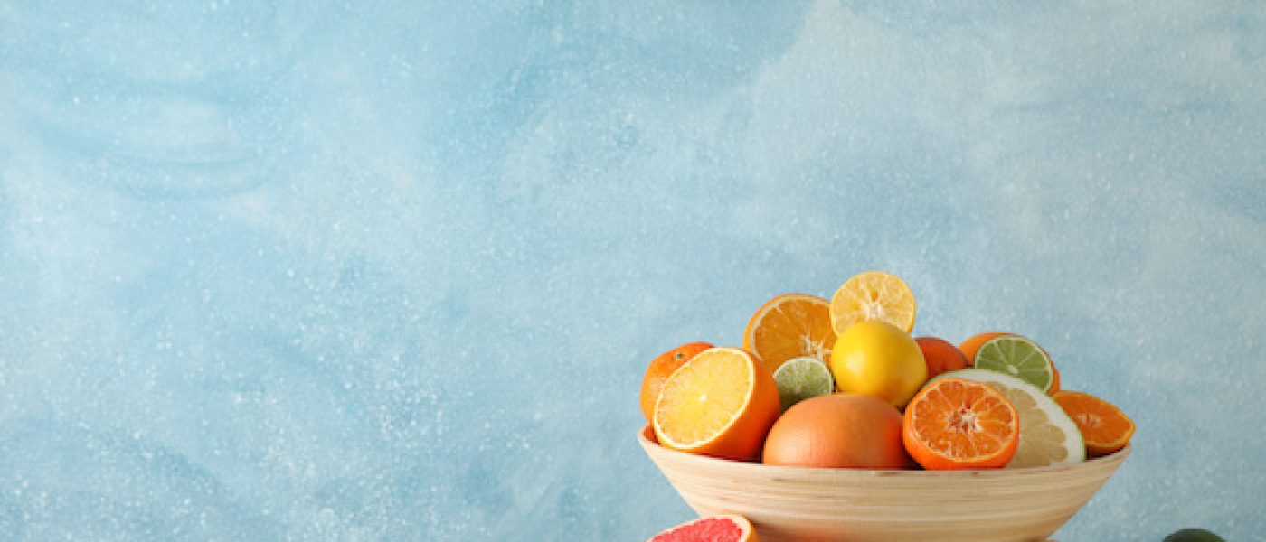 Juicy citrus fruits in bowl on wooden table against blue background, space for text