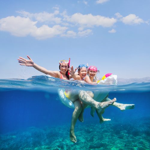 happy family with children is swimming and having fun in the sea on an inflatable mattress. View with above and below water