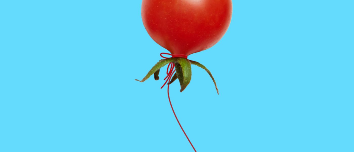 A red tomato balloon flying up on blue background